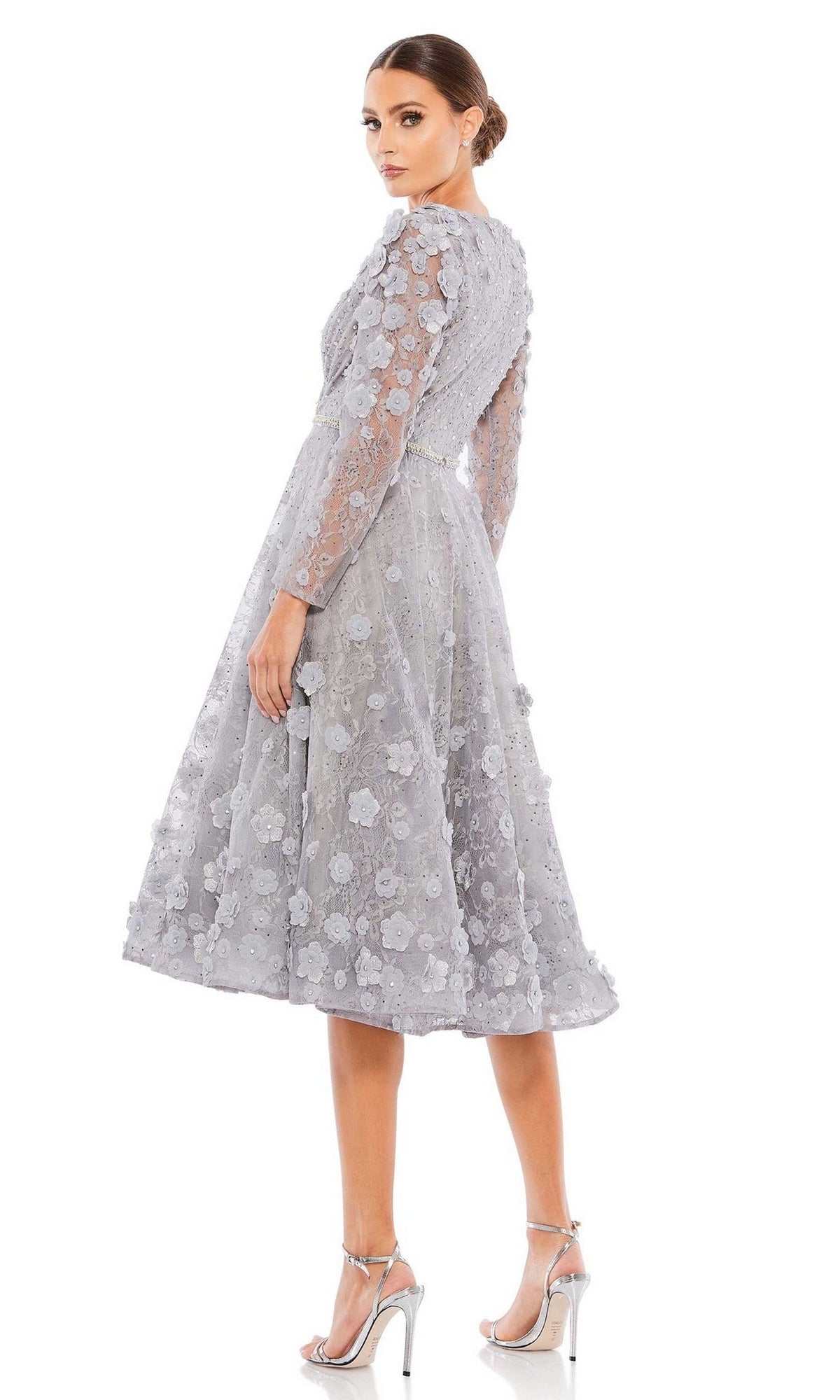 Woman wearing the Short Wedding Guest Dress 67387 by Mac Duggal, a light grey, tea-length dress with long sleeves and floral lace, paired with silver high-heeled sandals, standing against a white background.